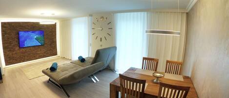 Ein modernes Wohnzimmer mit einer Couch, einem Esstisch und einem an einer Ziegelwand montierten Fernseher.