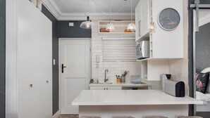 A modern kitchen with a white island, bar stools, pendant lights, and a clock on the wall. - Mouille Point Studio with Breathtaking Views (Cape Town)