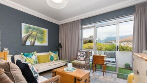 A living room with a sofa, chairs, a wooden coffee table, and a painting of a tree. - Mouille Point Studio with Breathtaking Views (Cape Town)