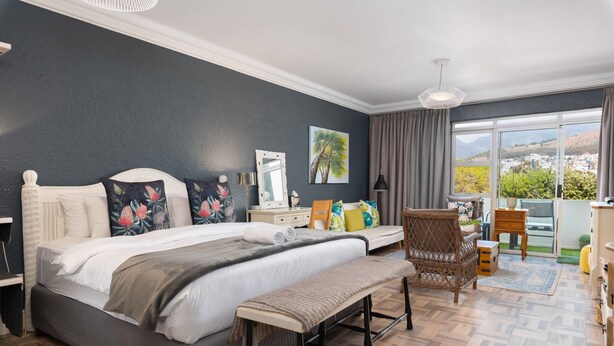 A bedroom with a large bed, a bench, a chair, and a view of the outside. - Mouille Point Studio with Breathtaking Views (Cape Town)