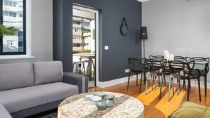A modern living room with a grey sofa, a round coffee table with decorative bowls, a dining area with chairs, and a view of a balcony with buildings. - Edgy Green Point Pad , Balcony , Parking , Pool (Cape Town)