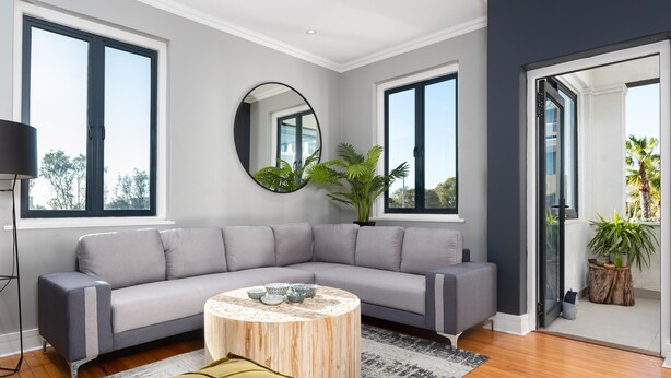 A modern living room with a grey sectional sofa, a round wooden coffee table, and a large mirror on the wall. - Edgy Green Point Pad , Balcony , Parking , Pool (Cape Town)