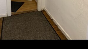 En gang med en dør der fører til et værelse, et gråt tæppe og tre røde valmuer som billeder på væggen.
