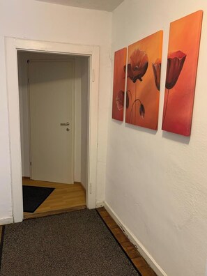 Käytävä, jossa on ovi, ovimatto ja kolme taulua seinällä.