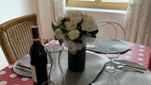 A dining table set with placemats, cutlery, a wine bottle, a glass, and a vase with white flowers.