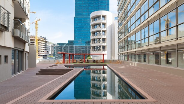 A modern building with a pool, large windows, and a view of a tall skyscraper in the background.