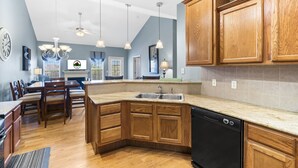 A kitchen with wooden cabinets, a dishwasher, and a dining area with chairs and a table. - Branson Vacation Rental | Game Room | Garage | Sleeps 8 (Branson)