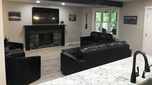 Ein modernes Wohnzimmer mit Kamin, einer schwarzen Ledersofa und einer Küchenzeile mit Granitarbeitsplatte.