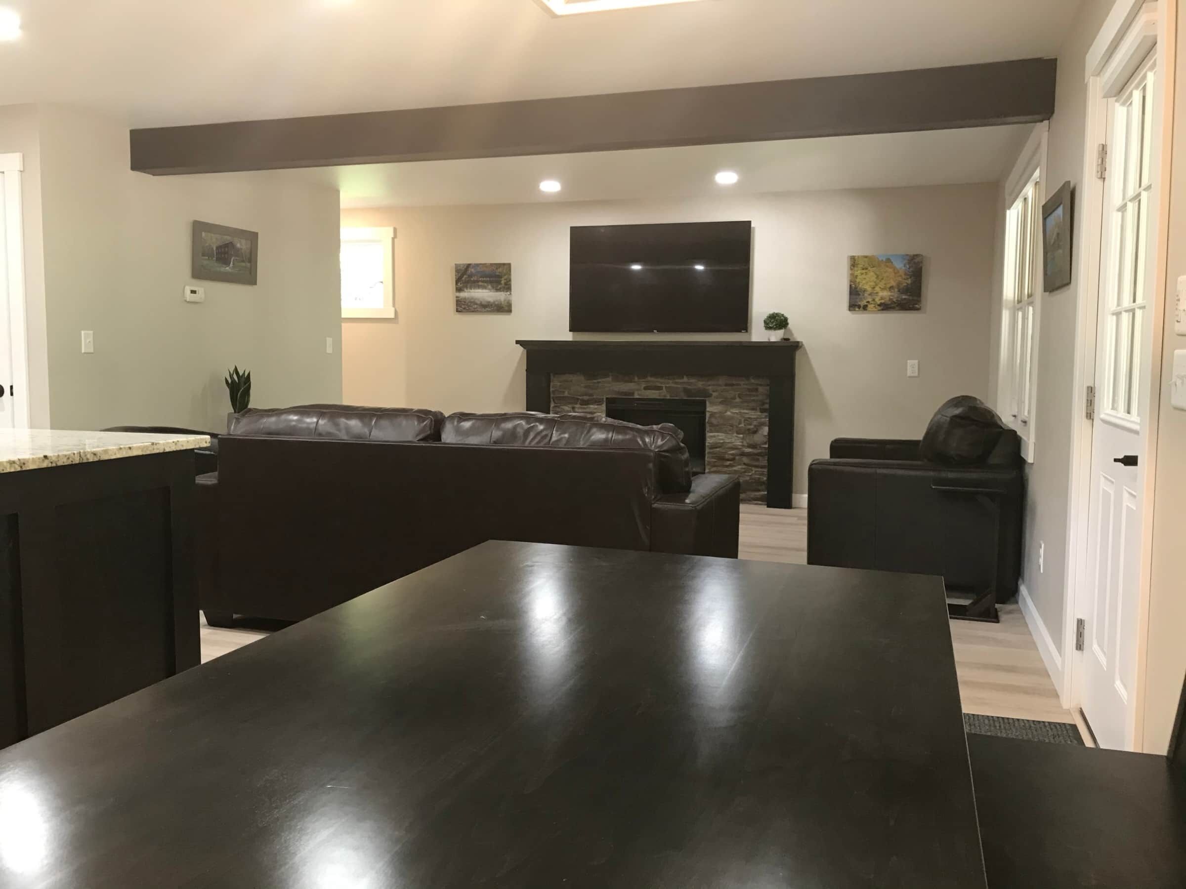 A modern living room with a dark wooden dining table, leather sofa, and a stone fireplace.
