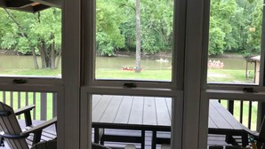 Blick von einer überdachten Terrasse mit großen Fenstern auf einen Fluss, umgeben von Bäumen.