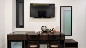 Ein modernes Hotelzimmer mit einem Wand-Fernseher, einem Holztisch mit zwei Stühlen, einer Kaffeemaschine und einer kleinen Vase mit Blumen.