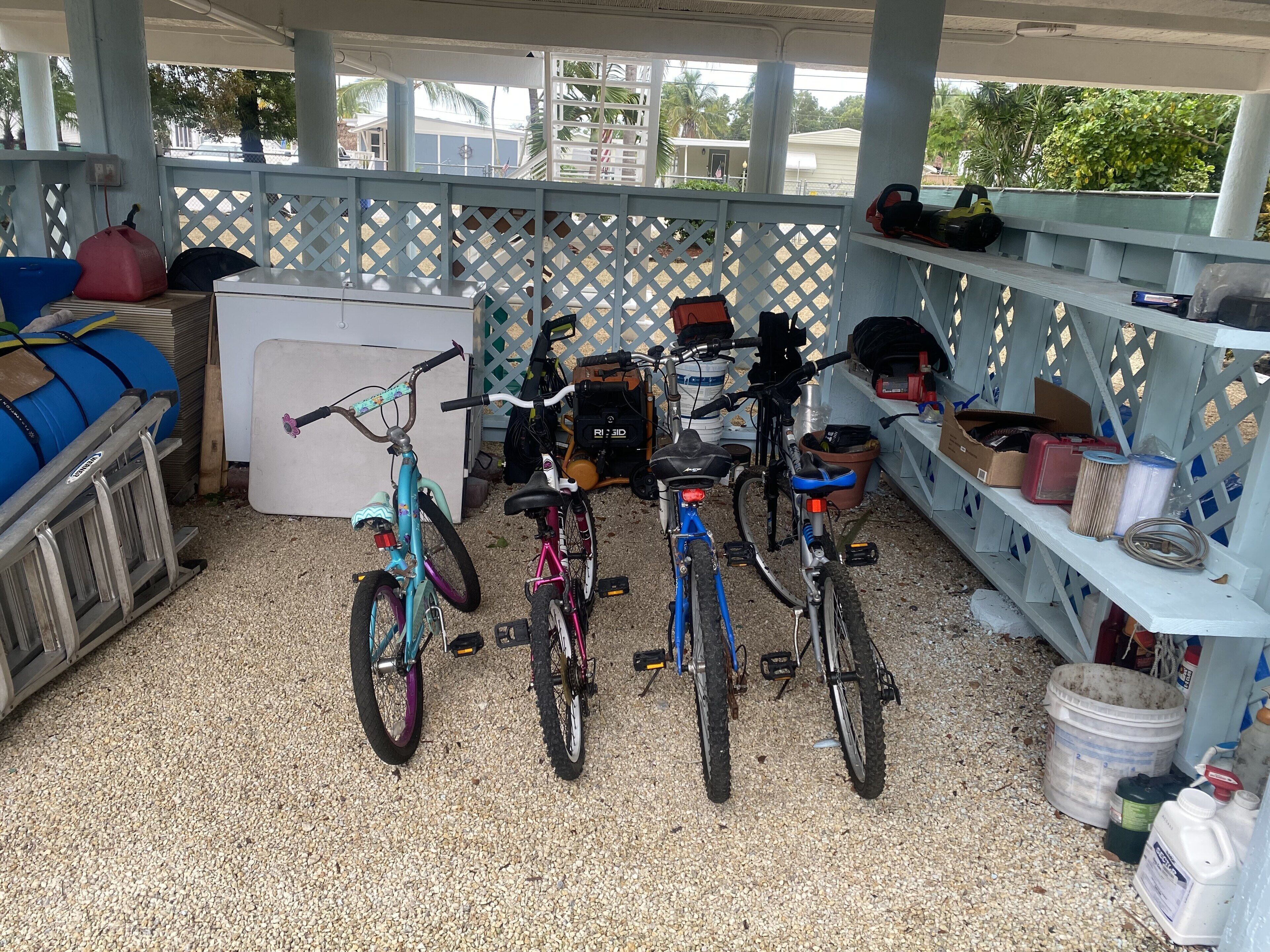 Un espacio al aire libre techado con bicicletas, un refrigerador blanco y diversas herramientas y provisiones.
