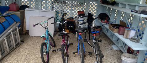 Un espacio al aire libre techado con bicicletas, un refrigerador blanco y diversas herramientas y provisiones.