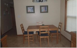 A dining area with a wooden table and chairs, two framed pictures on the wall, and a window with blinds. - ~Free Bike Rides - 3 miles from John Pennekamp - Your Happy Place~ (Key Largo)