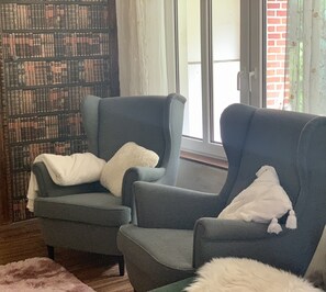 Zwei Sessel mit weißen Kissen, ein Bücherregal und ein Fenster mit Vorhängen.