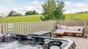 A hot tub with a wooden deck, a wooden fence, and a wooden bench with cushions.