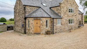 A stone house with a wooden door, a chimney, and a gravel driveway.