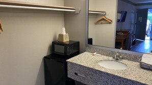Un baño pequeño con encimera de granito, un lavamanos, un espejo, un microondas y un refrigerador compacto.
