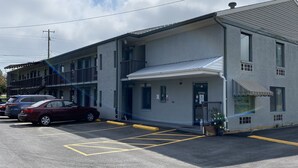 Un motel de dos pisos con estacionamiento, entrada cubierta y letrero de oficina a la vista.