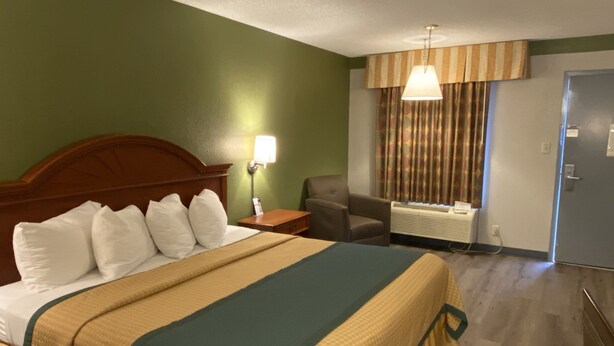 Habitación de hotel con una cama grande, una silla, un escritorio, una lámpara y una ventana con cortinas.