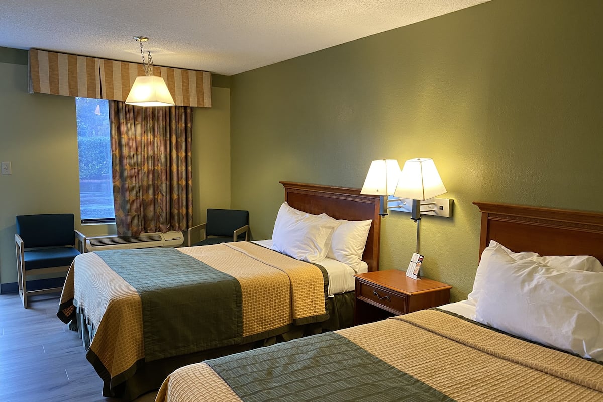 Ett hotellrum med två sängar, ett skrivbord, en stol och ett fönster med gardiner.