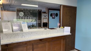 Un mostrador de recepción con un cartel que indica Best Value Inn, horario de atención y políticas como identificación requerida, no se admiten mascotas y una estancia máxima de 40 kilómetros.