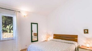 Ein Schlafzimmer mit einem Bett, einem Nachttisch, einem Spiegel und einem Fenster mit Vorhängen.