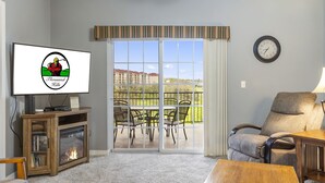 Ein Wohnzimmer mit Fernseher, Kamin, Sofa und Blick auf einen Balkon mit Gartenmöbeln.