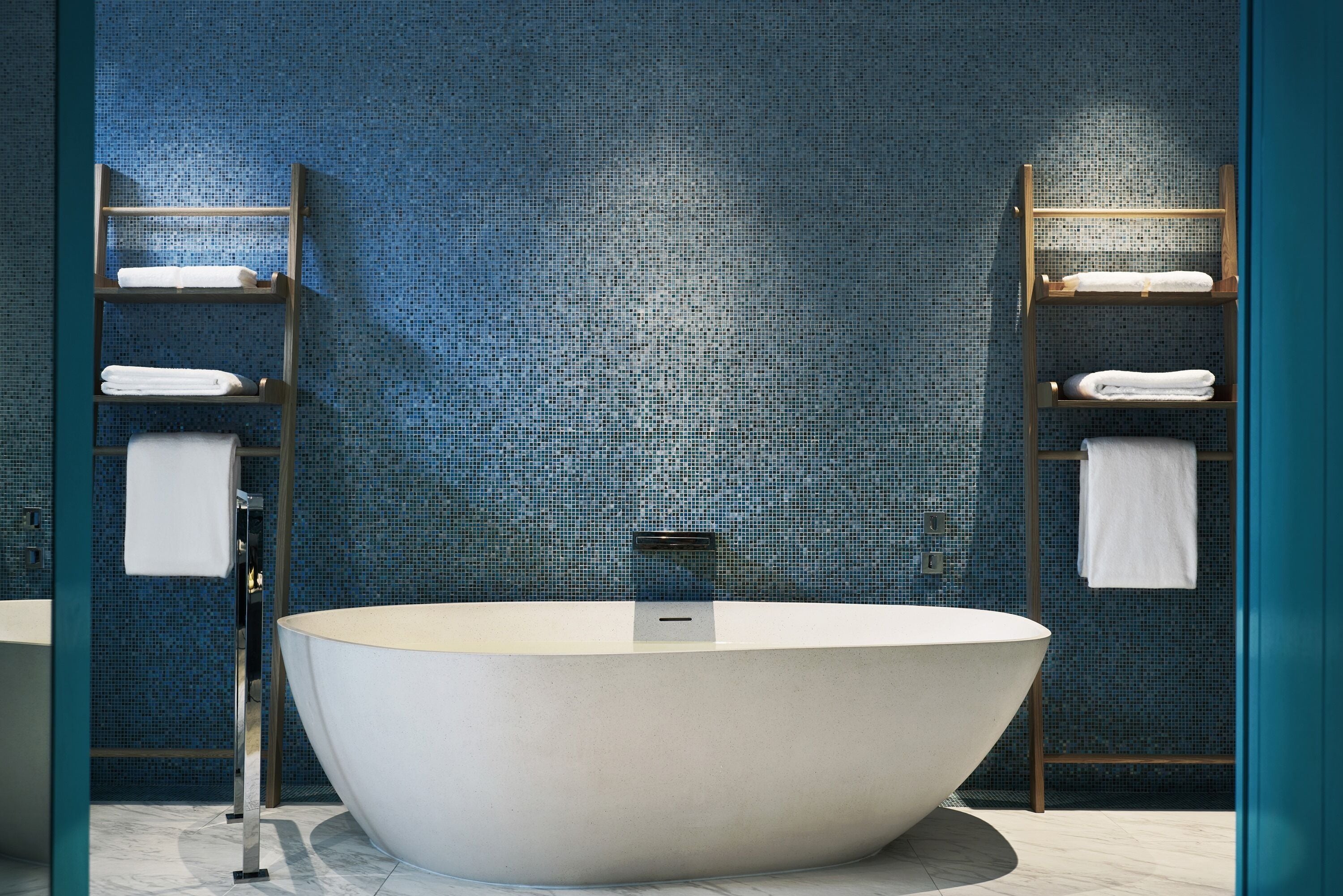 A modern bathroom with a freestanding bathtub, tiled walls, and wooden towel racks.