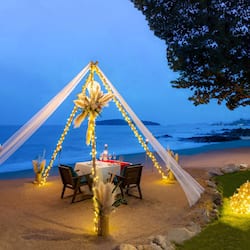 Romantic beach dining setup with a table, chairs, and a beautiful flower arrangement.