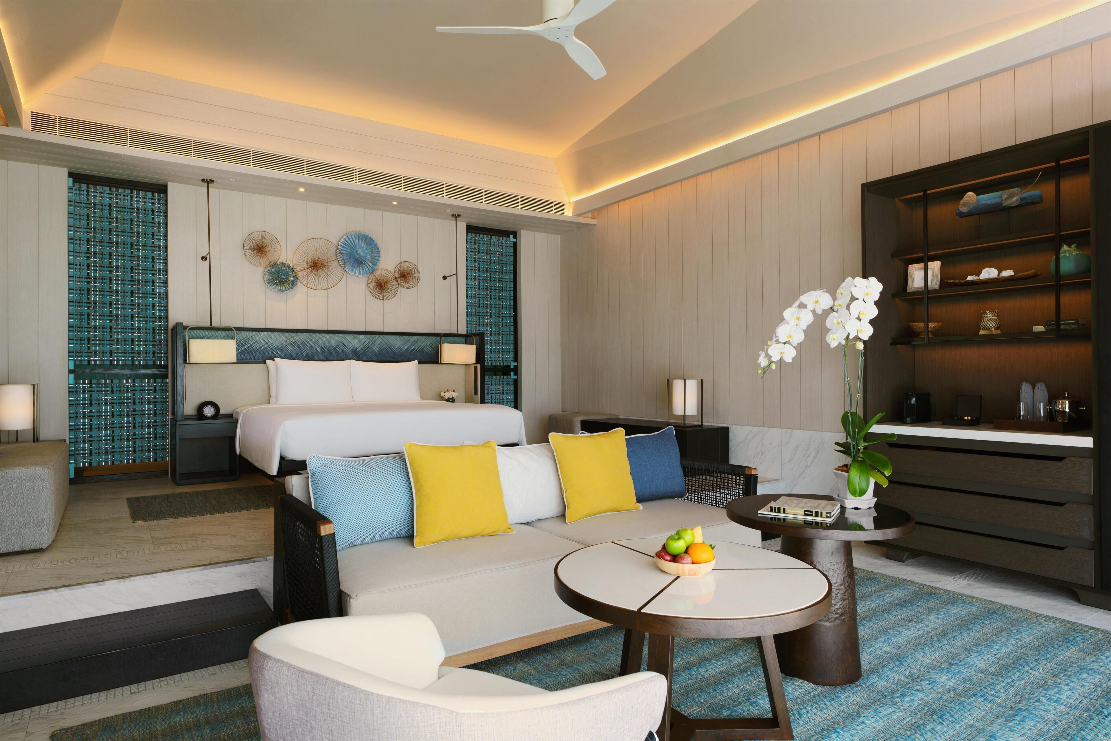 Una habitación de hotel moderna con cama, sofá, mesa de centro y una pequeña zona de comedor.