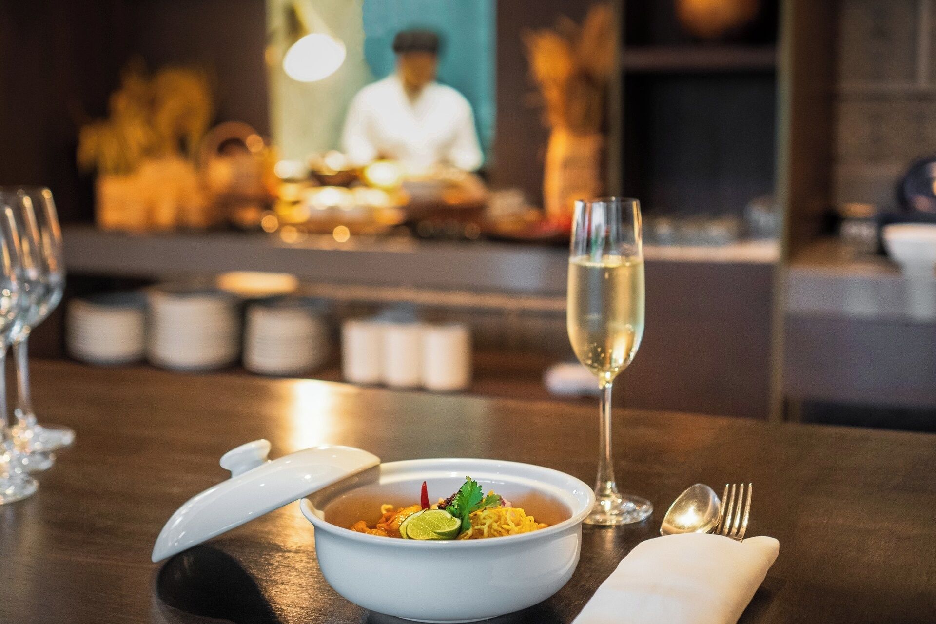 A dining table with a bowl of food, a glass of champagne, and cutlery.