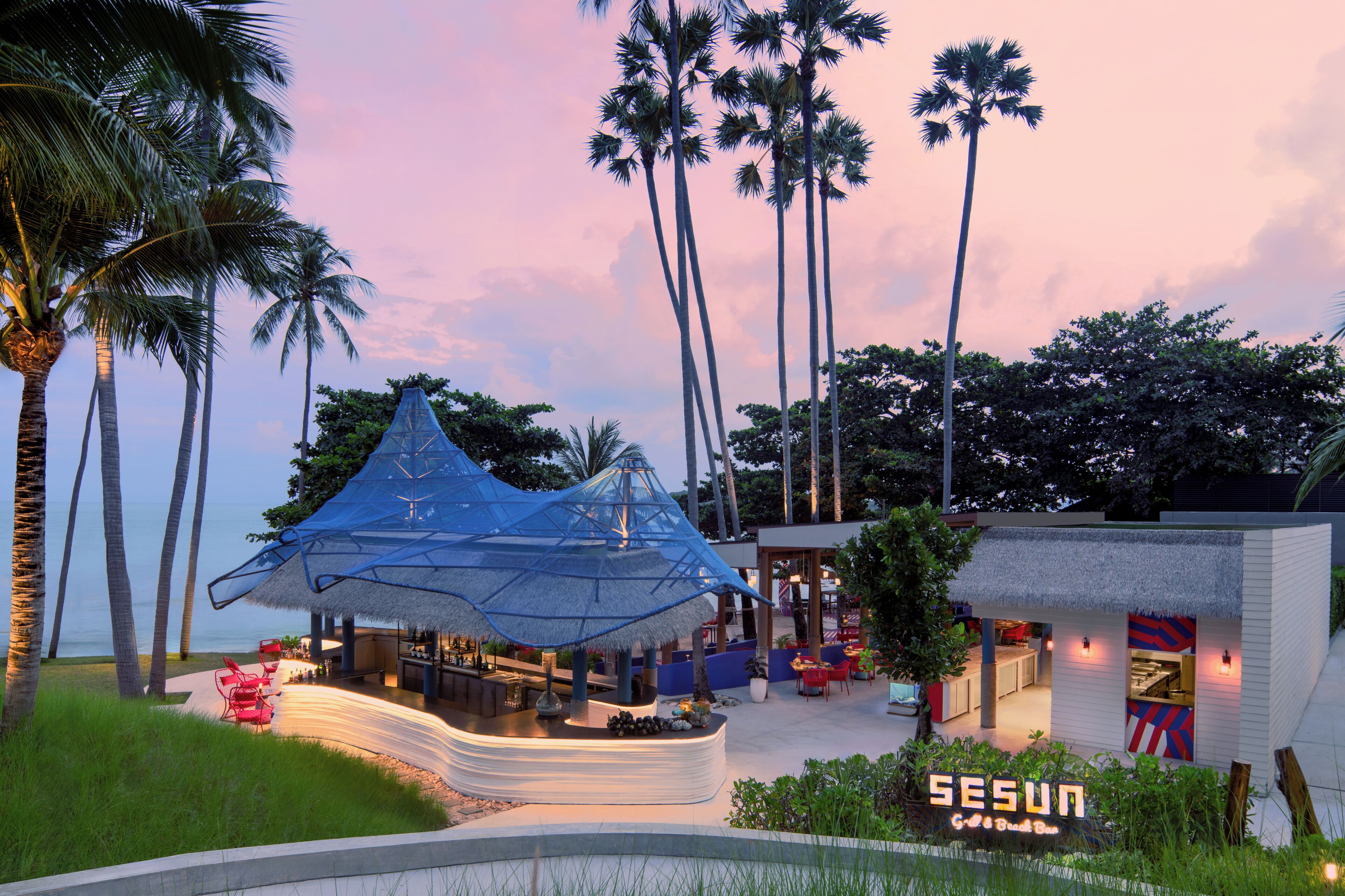 A beachside resort with a thatched-roof bar, palm trees, and a sign reading "SESUN".