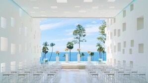 Montaje de ceremonia de boda con sillas dispuestas en filas, un escenario decorado con flores y vista al océano.