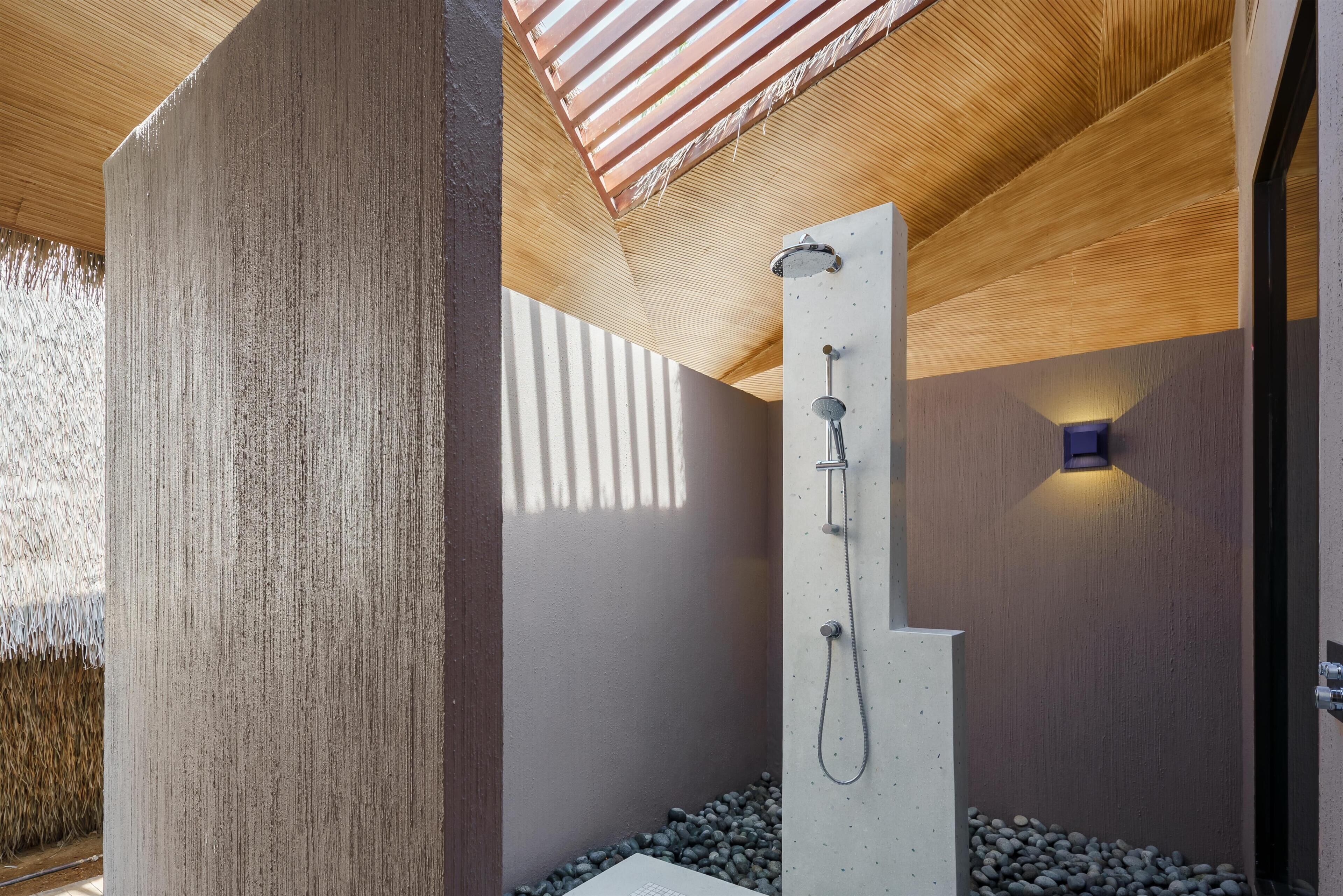 Un espace douche moderne avec un plafond en bois, un pilier en béton et une pomme de douche fixée au mur.