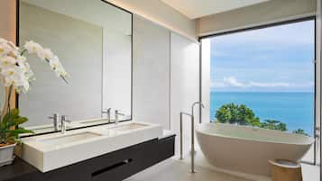 A modern bathroom with a dual sink vanity, a freestanding bathtub, and a large mirror reflecting a view of the ocean.
