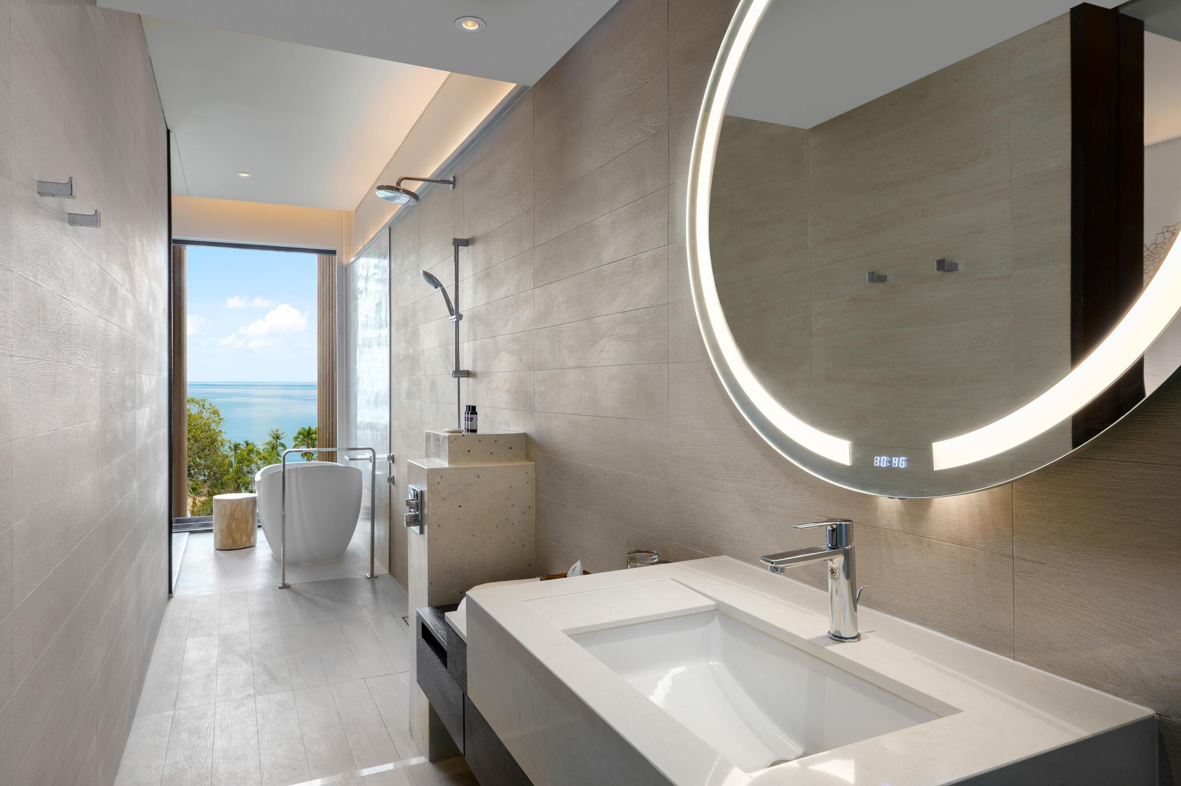 Une salle de bain moderne avec un grand miroir, une baignoire et une vue sur la mer.
