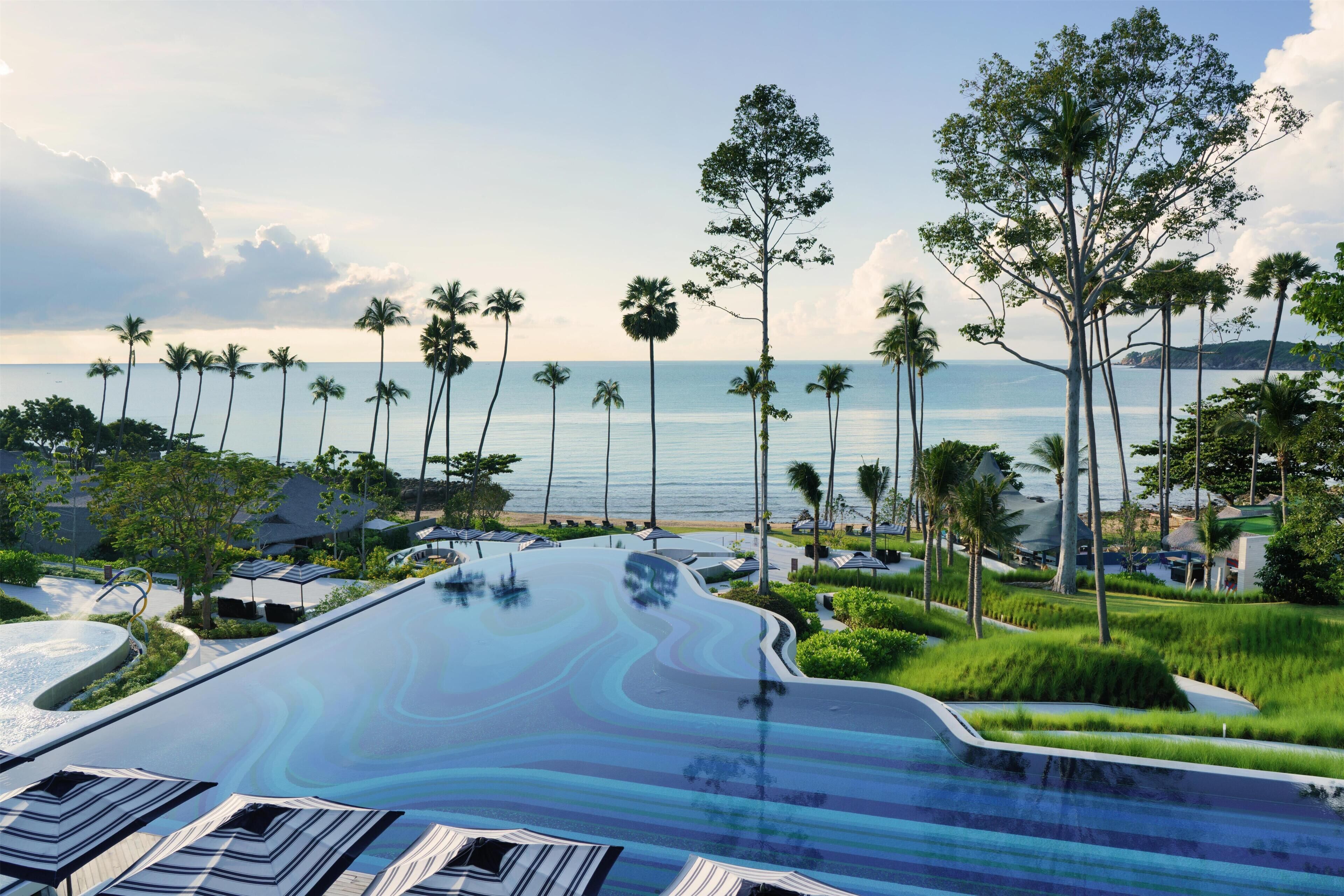 Un resort con piscina, palmeras y vista al océano.