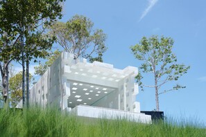 A modern building with a geometric design, surrounded by tall grass and trees.