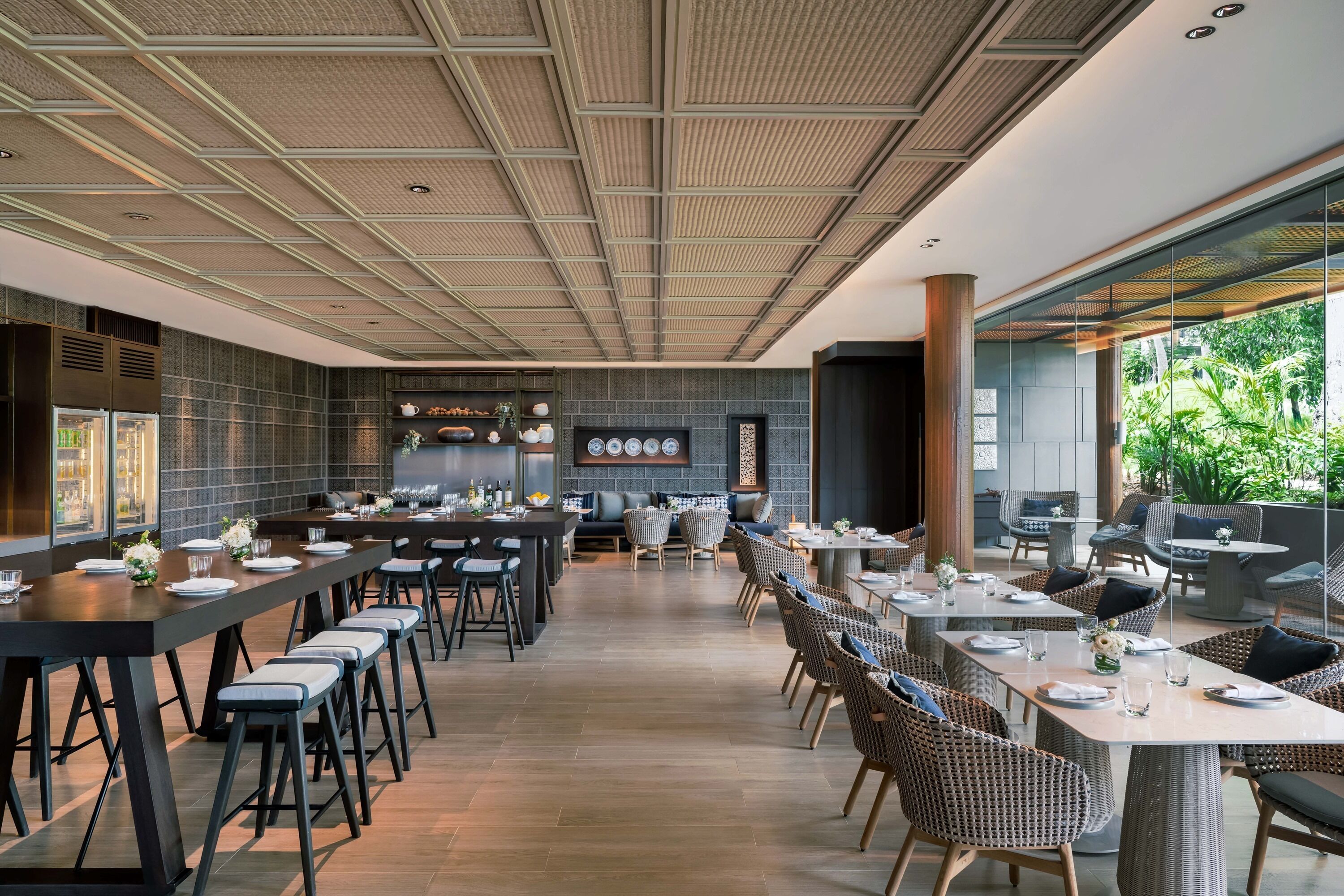 Un restaurant moderne doté d’une grande table conviviale, de tables individuelles et offrant une vue sur la verdure environnante.