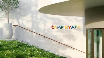 A modern building with a staircase leading to a glass door, a large planter, and the text 'CAMP HYATT' on the wall.