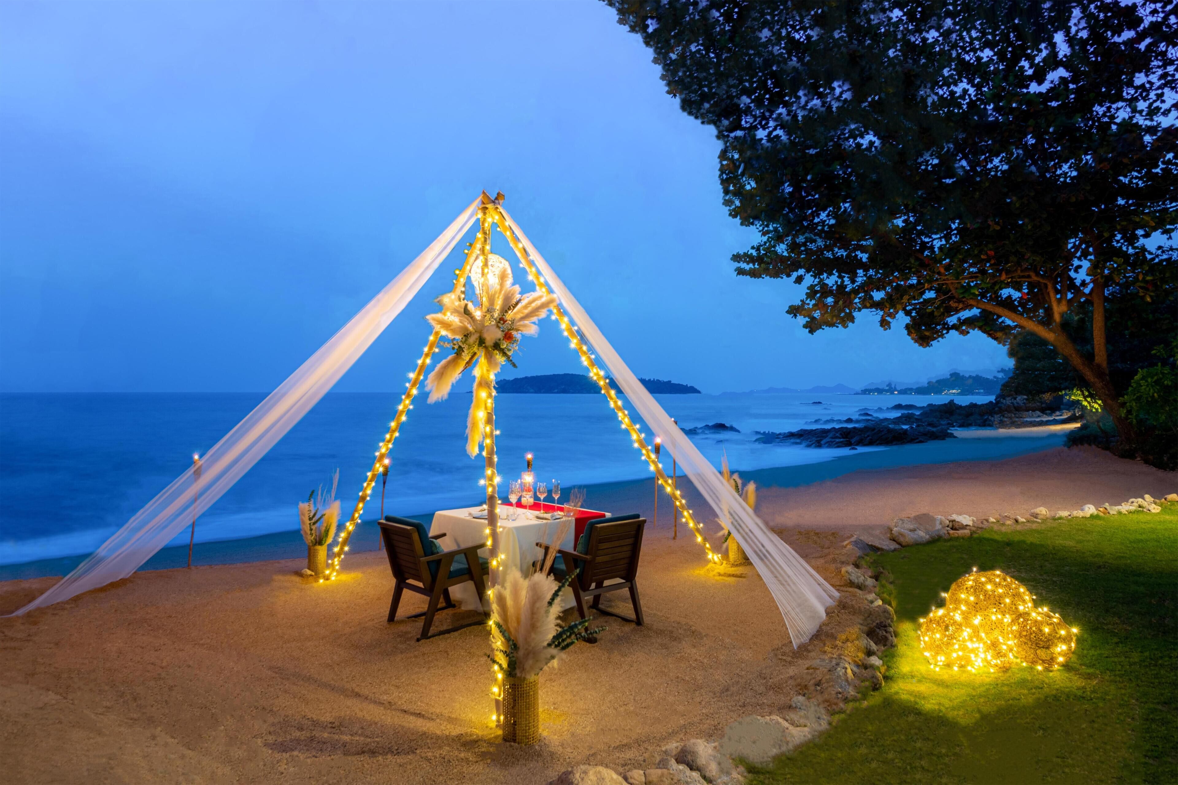 Montaje para comer frente al mar con una mesa, sillas y luces colgantes.