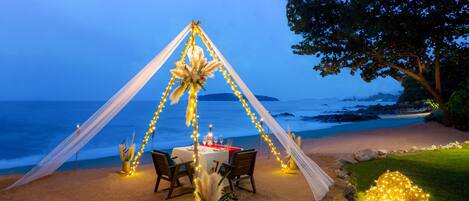 Montaje para comer frente al mar con una mesa, sillas y luces colgantes.