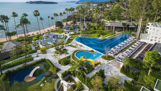 Un resort con una amplia piscina, playa y montañas al fondo.