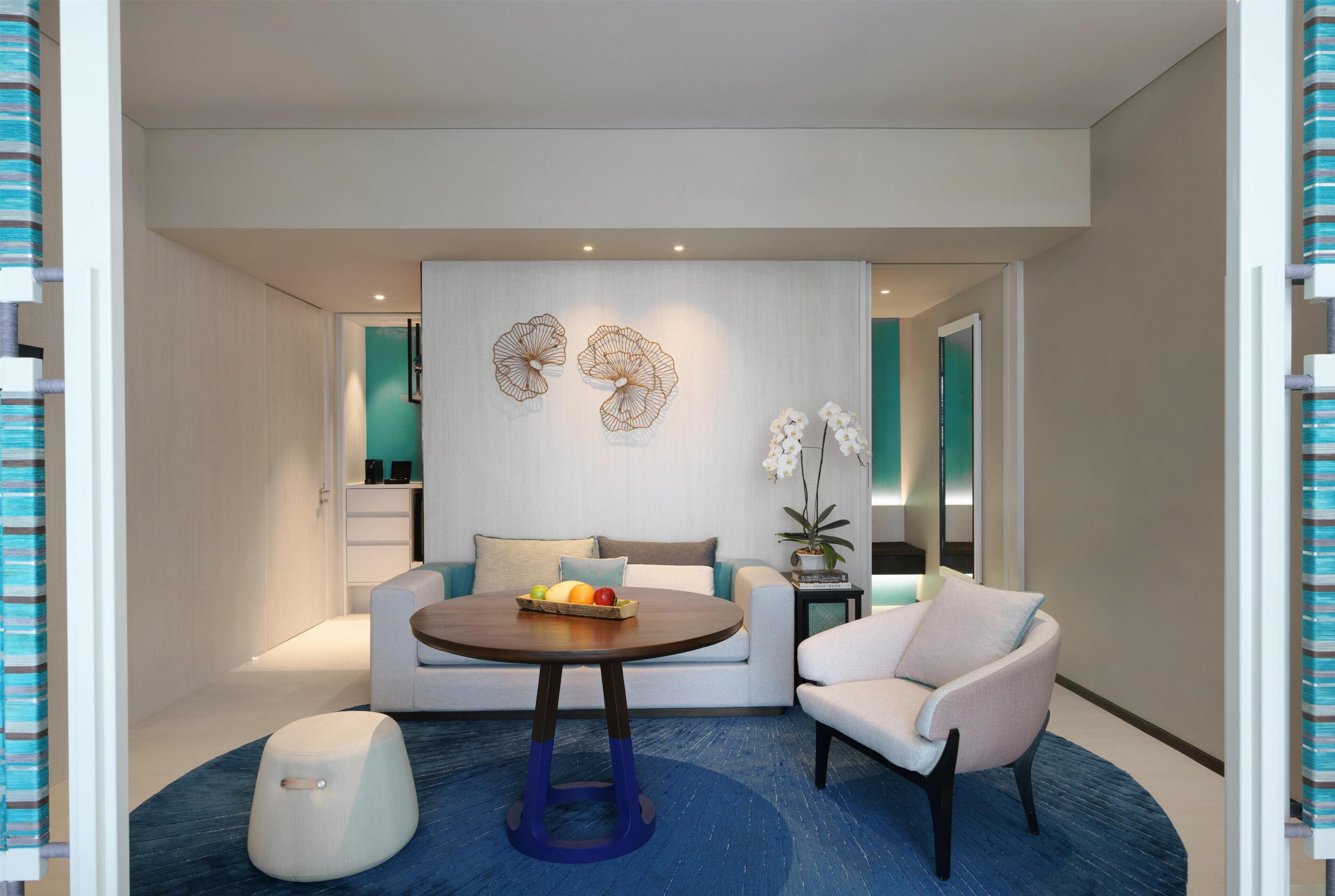 A modern living room with a round table, sofa, and armchair, a blue carpet, and decorative wall art.