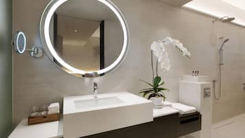 A modern bathroom with a large mirror, a sink, a shower, and a potted orchid.