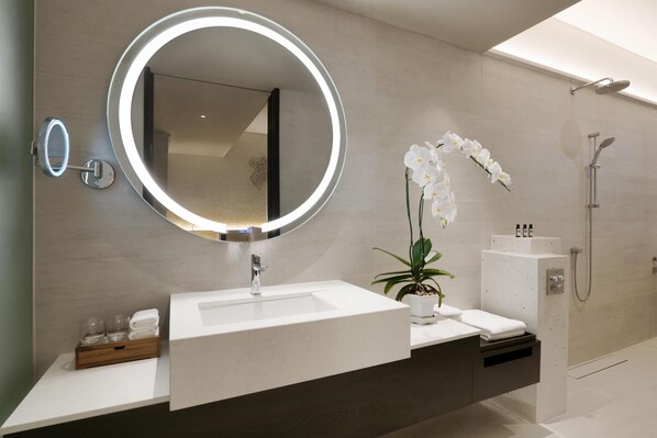 A modern bathroom with a large mirror, a sink, a shower, and a potted orchid.