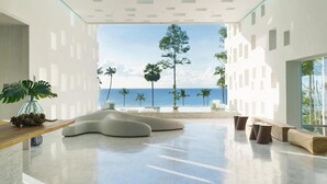 Un interior moderno con vista al océano, que incluye una zona de estar curvo, una mesa de madera con una planta y un gran ventanal.