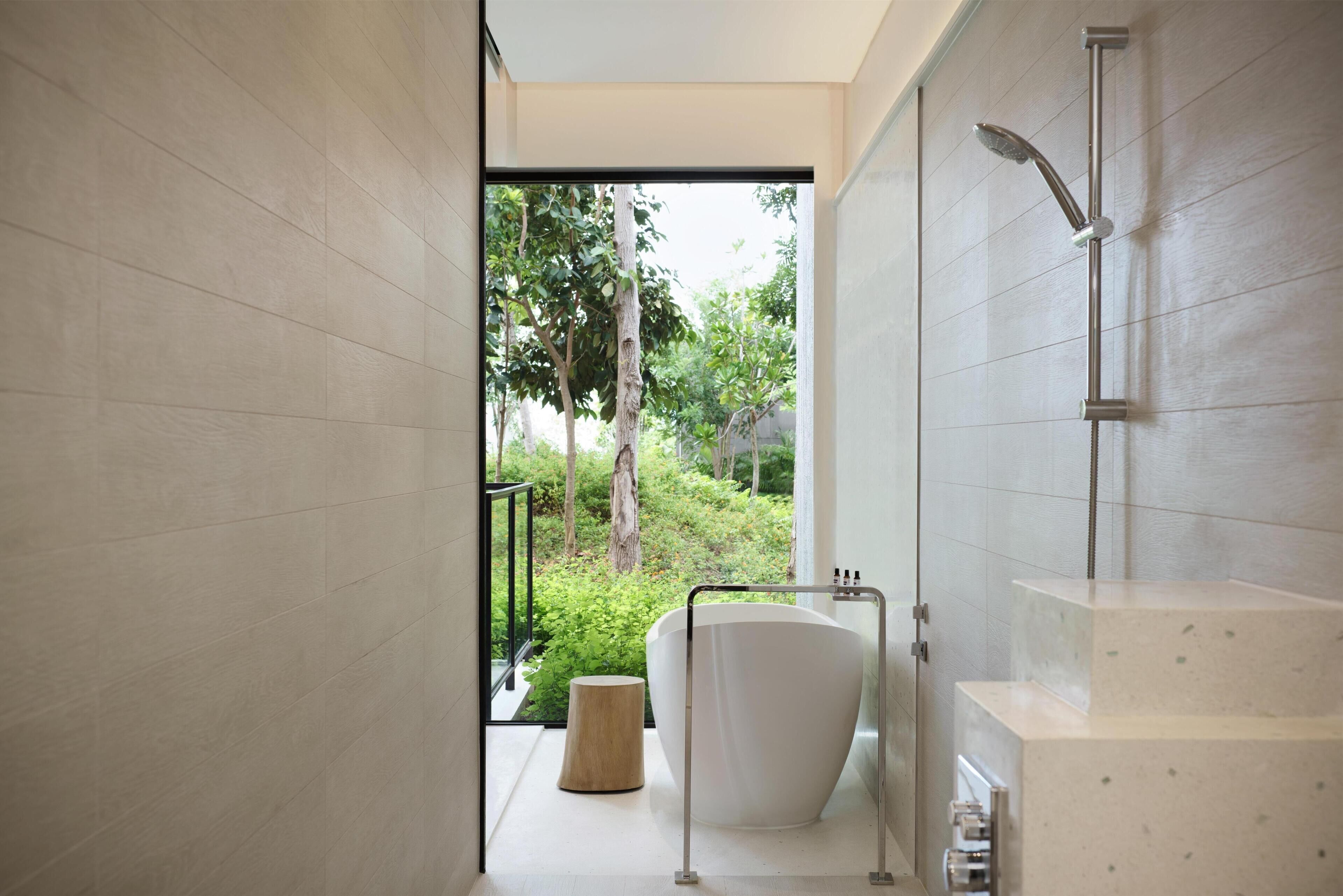 Un baño moderno con una bañera independiente, un cabezal de ducha y vistas al exterior con vegetación.