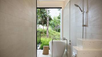 Un baño moderno con una bañera independiente, un cabezal de ducha y vistas al exterior con vegetación.